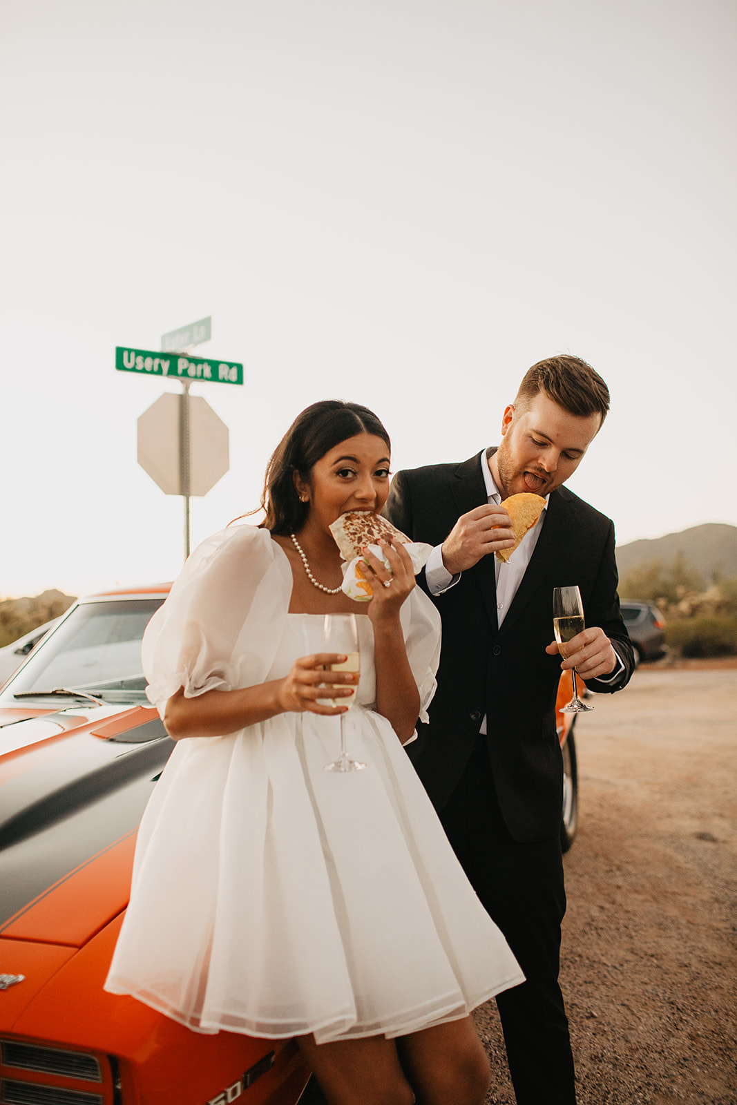 couples eating taco bell in front of a vintage car while holding champagne