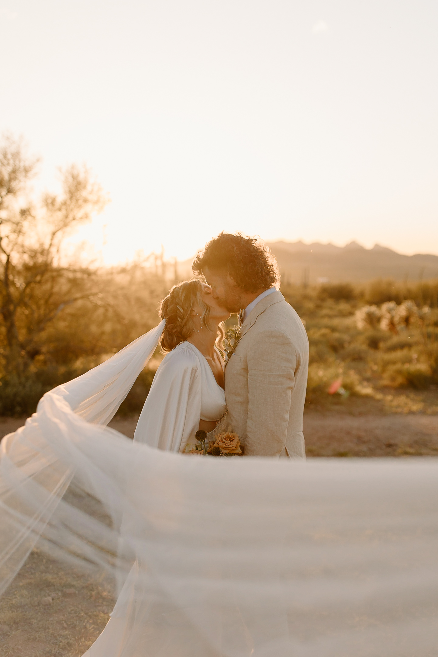 wedding portrait of a bride and groom in the desert with veil blowing in the wind.